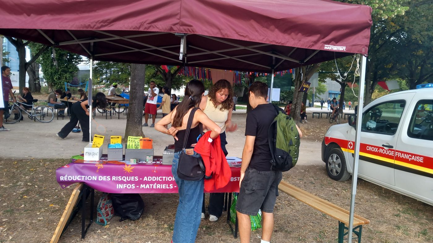 Le stand de réduction des risques des Étudiant.e.s Relais Addicto sous un barnum, dans un parc, avec des étudiant.e.s qui se renseignent