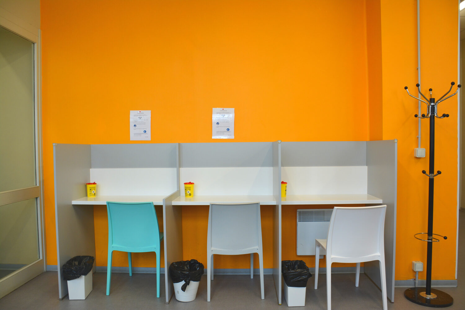 L’espace de consommation supervisé d’Argos : trois postes séparés par des cloisons, devant un mur orange